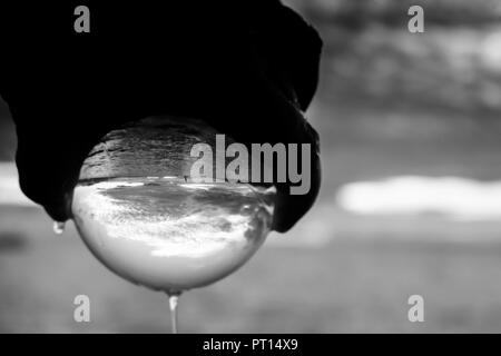 Coucher de soleil paysage marin noir et blanc capturé dans le verre ballon tenu dans la main avec l'écoulement d'eau Banque D'Images