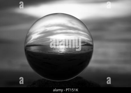 Le noir et blanc sunset seascape de bougies sur l'eau capturée dans close up bille de verre ou globe terrestre Banque D'Images