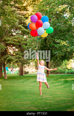 Happy little girl Playing with gros bouquet de ballons colorés remplis d'hélium dans le parc Banque D'Images