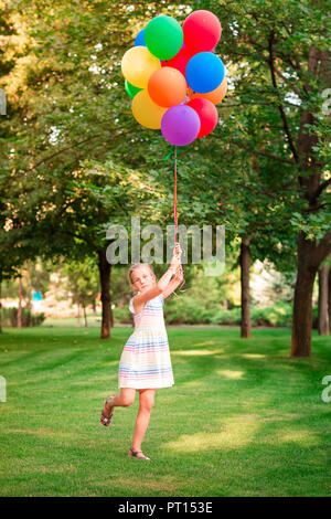 Happy little girl Playing with gros bouquet de ballons colorés remplis d'hélium dans le parc Banque D'Images