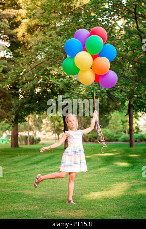 Happy little girl Playing with gros bouquet de ballons colorés remplis d'hélium dans le parc Banque D'Images