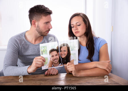 Sad Young Couple Holding leur photographie déchirée sur un bureau en bois Banque D'Images