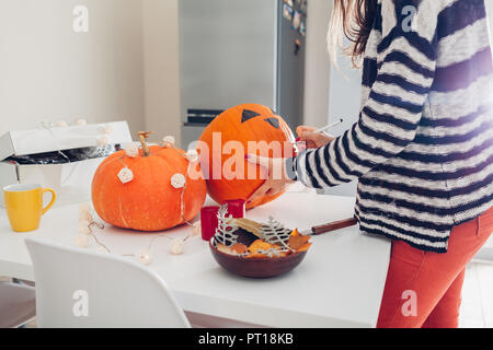 Young woman making jack-o-lanterne pour halloween sur cuisine. Dessiner les yeux, le nez et la bouche avec un crayon sur la citrouille. La préparation de décoration pour maison de vacances Banque D'Images