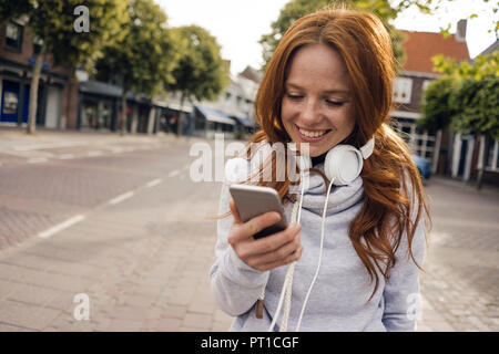 Femme rousse avec un casque et un téléphone intelligent dans la ville Banque D'Images