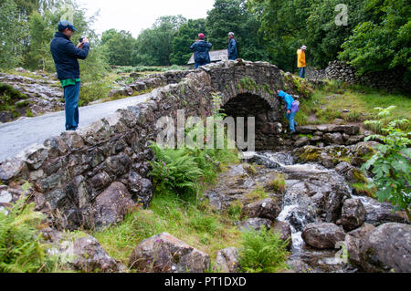 Les gens se tenant sur les petits pont voûté en pierre appelée Ashness Pont sur une course rapide et rocky stream de descendre vers Derwent Water en Cumbria. Banque D'Images