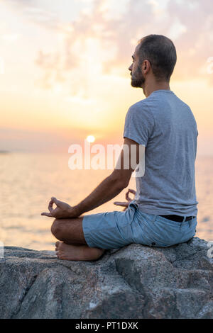 L'Espagne. Homme méditant au lever du soleil, on Rocky beach Banque D'Images