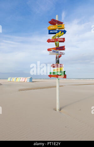 Panneau avec les directions vers des destinations internationales à la plage de Berck-Plage, France, cabines de plage colorées en arrière-plan. Banque D'Images