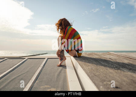 Woman with tattoo accroupi sur planche, regardant la mer Banque D'Images