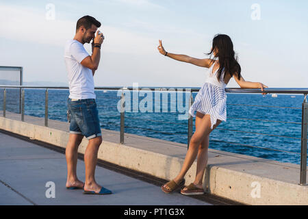 Jeune couple urbain par la mer, la femme faisant la paix sign Banque D'Images