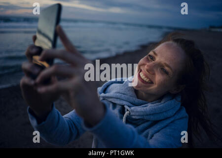 Femme à l'aide du smartphone sur la plage au coucher du soleil Banque D'Images