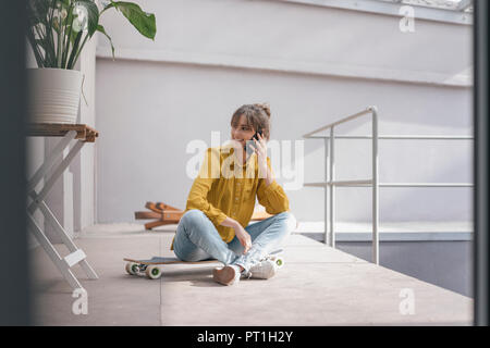 Jeune femme assise sur la planche à roulettes, using smartphone Banque D'Images
