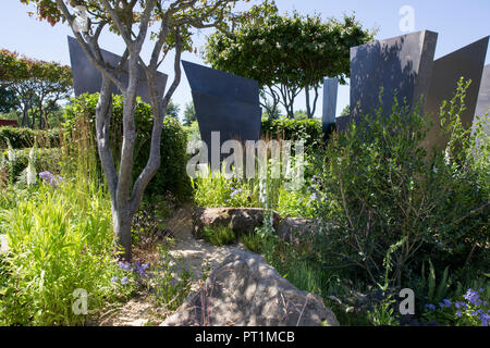 Vue sur le jardin moderne contemporain avec de grandes palmes sculpturales en bronze, et de grands blocs de pierre, plantation de Digitalis purpurea F. albiflora Banque D'Images