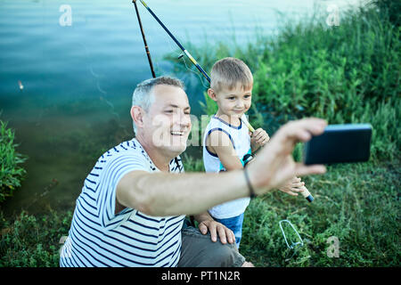 Grand-père et petit-fils en tenant au lakeshore smartphone avec selfies Banque D'Images