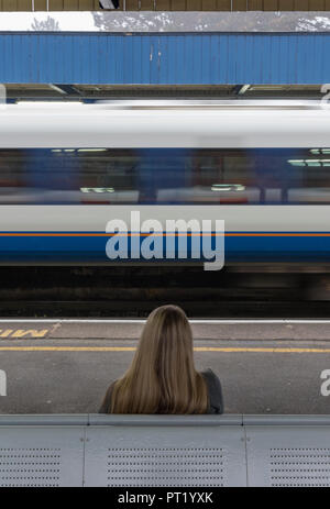 jeune femme assise seule à une gare avec un train passant à vitesse, attendant un train, le trajet quotidien, jeune femme assise sur banc à plate-forme de la gare. Banque D'Images