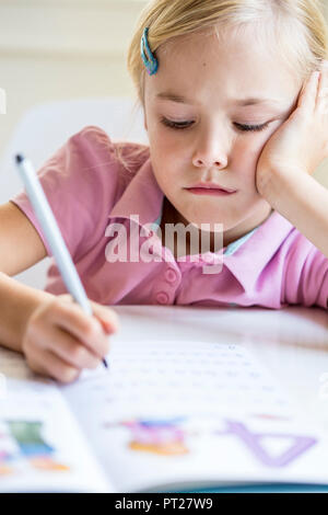 Portrait de petite fille s'ennuie l'écriture des chiffres dans un livre d'exercices Banque D'Images