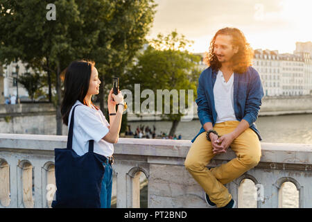 France, Paris, jeune femme de prendre une photo de son petit ami à Seine au coucher du soleil Banque D'Images