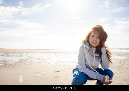 Femme rousse de détente sur la plage, accroupi Banque D'Images