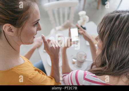 Deux copines à une réunion dans un café-restaurant, using smartphone Banque D'Images