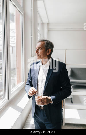 Mature businessman avec verre de café dans son bureau à la fenêtre de Banque D'Images