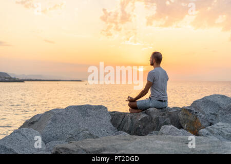 L'Espagne. Homme méditant au lever du soleil, on Rocky beach Banque D'Images