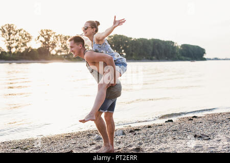 Young man giving girlfriend piggyback ride à la rive Banque D'Images