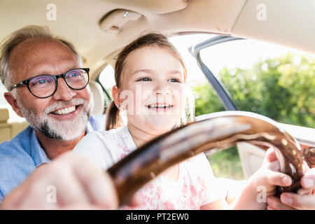 Petite fille assise sur les genoux de grand-père, faisant semblant de diriger la voiture Banque D'Images