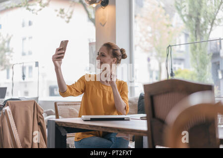 Jeune femme assise dans l'espace de coworking, selfies smartphone Banque D'Images