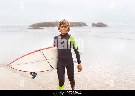 L'Espagne, Aviles, jeune surfer carrying surfboard on the beach Banque D'Images