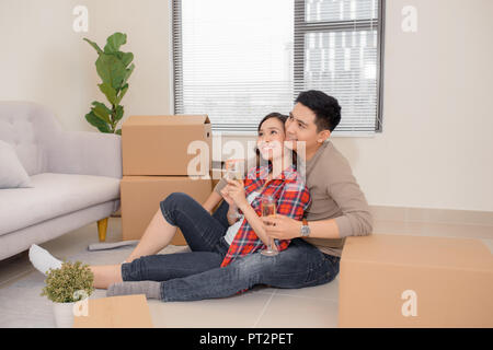 Close-up shot of Asian couple joyeux tintement des verres à vin ensemble tout en étant assis sur le plancher du nouvel appartement Banque D'Images