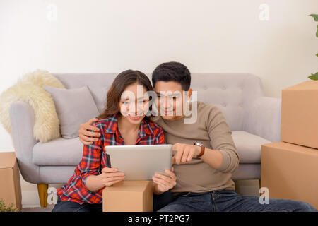 Happy young couple petites annonces décisions projet futur internet avec ordinateur à la maison tandis que les boîtes d'emballage et de déménagement Mobilier lors entrer dans le Banque D'Images