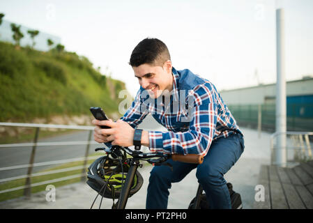 Smiling Young man with bicycle looking at smartphone Banque D'Images