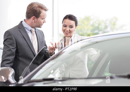 Au concessionnaire, vendeur montrant nouvelle voiture au client Banque D'Images