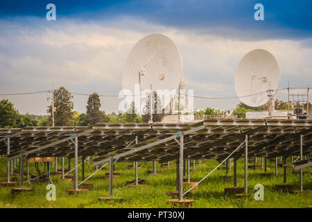 Blanc à grande échelle double antenne satellite dans le cadre de la ferme solaire bleu dramatique et ciel nuageux fond. Banque D'Images