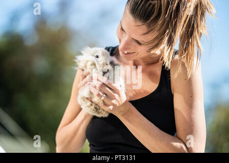 Young smiling woman holding baby rabbit fourrure dans ses mains à l'extérieur par une journée ensoleillée. Banque D'Images