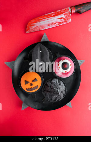 Black Lips avec des crocs de vampire, une déchirure de l'oeil, un inquiétant la citrouille et la montagne noire. Scary Halloween à la citrouille Gâteau mousse sur un fond de couleur rouge, vue du dessus avec le sang du couteau. Banque D'Images