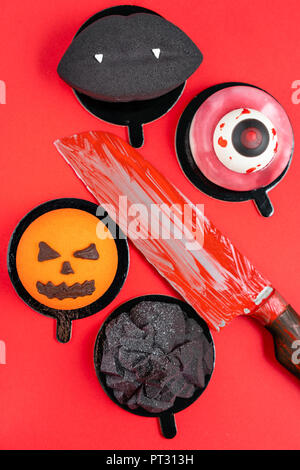 Black Lips avec des crocs de vampire, une déchirure de l'oeil, un inquiétant la citrouille et la montagne noire. Scary Halloween à la citrouille Gâteau mousse sur un fond de couleur rouge, vue du dessus avec le sang du couteau. Banque D'Images