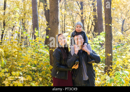 Les gens, la famille et les loisirs concept - happy father holding petite fille sur le dos à l'automne park et la mère Banque D'Images