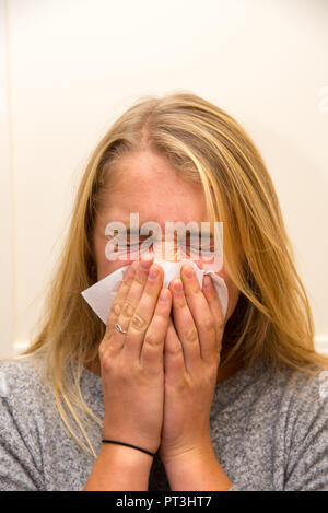 une jeune femme éternuant le nez avec un mouchoir
