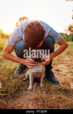 Balades et maître hugging dog pug en forêt d'automne. Chiot heureux assis sur l'herbe. L'amour de chien. Meilleurs amis Banque D'Images