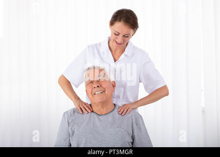 Jeune femme Massage Physiothérapeute Senior Man's Shoulder In Clinic Banque D'Images
