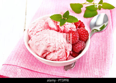 La crème glacée à la framboise rouge et menthe baies en blanc bol, une cuillère sur serviette rose sur planche de bois contexte Banque D'Images
