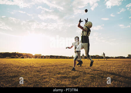 Jeune joueur de football américain qui reçoit une passe au cours de la pratique de l'équipe sur un terrain de football dans l'après-midi Banque D'Images