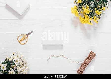Processus d'emballage de cadeaux faits à la main pour les vacances sur table en bois blanc, vue du dessus. Télévision lay présent vierge située en regard de bouquets de fleurs jaunes, Banque D'Images