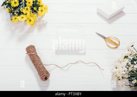 Mise à plat blanc blanc présente les cases en regard des bouquets de fleurs jaune or, des ciseaux et de la ficelle. Processus d'emballage de cadeaux faits à la main pour les vacances Banque D'Images