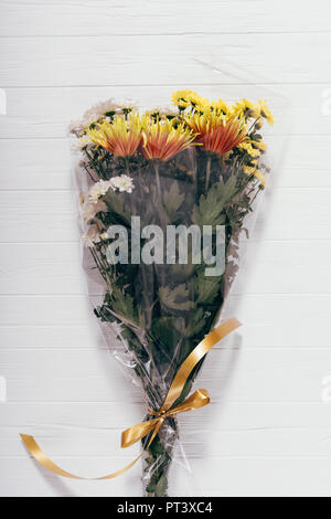 Long luxuriant bouquet d'asters jaune et orange emballées dans du cellophane transparent avec noeud. Vertical image cadeau frais de fleurs sur table en bois blanc, t Banque D'Images