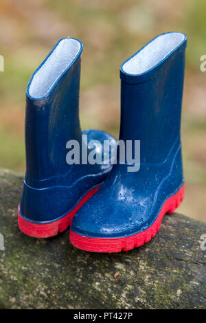 Childs un paire de petites bottes bleu avec semelles rouges laissées par un enfant dans un parc de pays. Banque D'Images