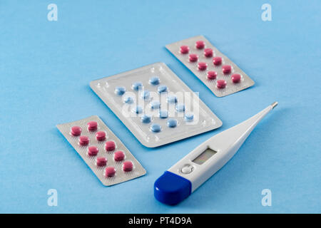 Les blisters de comprimés bleus et roses et thermomètre digital électronique sur fond bleu- santé et concept médical Banque D'Images