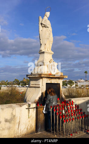 Cordoue, Espagne - 27 Février 2017 : une femme inconnue allume une bougie à la statue de l'Archange Gabriel sur le Pont Romain. Banque D'Images