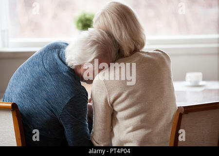 Vue arrière de l'arrière à la retraite senior homme aux cheveux gris se penchant sur l'épaulement de la femme d'amour mature pleurer ou rire, couple d'âge moyen plus âgés le collage, trus Banque D'Images