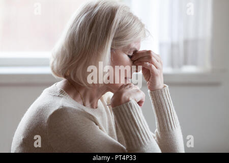Fatigué d'âge moyen en colère femme plus âgée, pont de nez massage sensation oculaire ou maux de tête d'essayer de soulager la douleur, triste dame mature senior épuisé d Banque D'Images